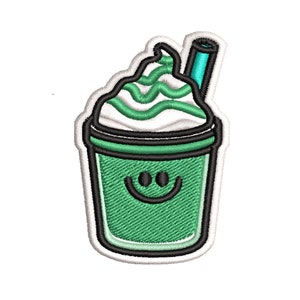 K&ouml;nnte beinhalten: Gr&uuml;ne und wei&szlig;e gestickte Applikation eines l&auml;chelnden gr&uuml;nen Smoothies mit Schlagsahne und einem blauen Strohhalm.