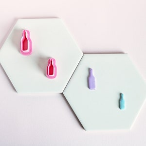 Peut inclure: Quatre emportes-pièces en forme de bouteilles de différentes tailles. Les emportes-pièces sont roses, violets et bleus. Les emportes-pièces sont disposés sur un fond blanc.