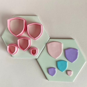 May include: Set of pink fondant cutters and pink, purple, blue and white fondant shapes on a green background.