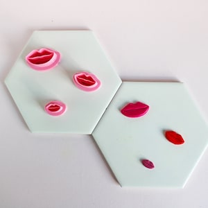 Peut inclure: Six emporte-pièces en forme de lèvres de différentes tailles, en rose et rouge, sur un fond blanc.