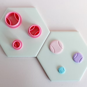 May include: Five different sized fondant cutters in the shape of a tennis ball. The cutters are pink, purple, and blue.