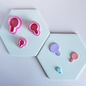 May include: Five pink and purple plastic cookie cutters shaped like light bulbs and keys on a white background.