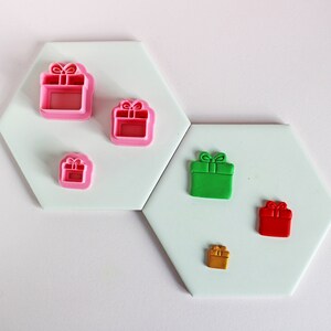 Peut inclure: Ensemble de six emporte-pièces en plastique de différentes tailles en forme de cadeaux. Les emporte-pièces sont roses, verts, rouges et dorés.