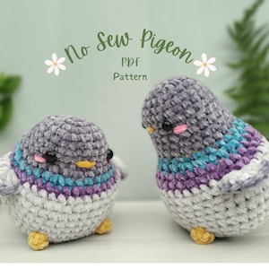May include: Two crocheted plush pigeon toys, one grey with a blue and purple stripe, the other grey with a blue, purple, and white stripe. The toys are on a white surface with green foliage in the background. The text "No Sew Pigeon PDF Pattern" is above the toys.