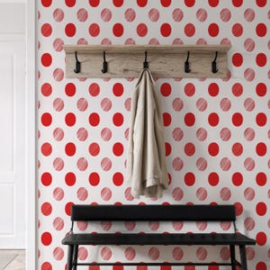 May include: A white wall with a red polka dot pattern. A wooden shelf with black hooks is mounted on the wall, with a beige coat hanging from one of the hooks. A black bench sits below the shelf.