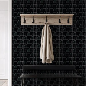 Könnte beinhalten: Moderner Eingangsbereich mit schwarz-weiß gemusterter Tapete. Eine Garderobe aus Holz mit schwarzen Haken ist an der Wand befestigt, an der ein beiger Mantel hängt. Darunter befindet sich eine schwarze Bank.