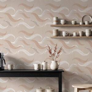 Puede incluir: Papel pintado de tonos neutros con un patrón repetitivo de pinceladas abstractas en blanco y tonos melocotón. La escena incluye una mesa negra con cafetera, taza y piezas de servicio, y estantes de madera con vajilla.
