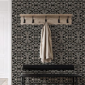 Könnte beinhalten: Ein beiger Mantel hängt an einer Wandgarderobe aus Holz mit schwarzen Haken. Die Wand hat ein geometrisches Muster in Schwarz und Creme. Unter der Garderobe befindet sich eine schwarze Bank, die einen funktionalen Eingangsbereich schafft.