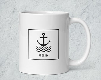 Pode incluir: Caneca de cerâmica branca com um design de âncora e ondas pretas. A palavra "MOIN" está impressa abaixo da âncora.