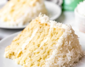 May include: A slice of white cake frosted with white frosting and covered in shredded coconut.