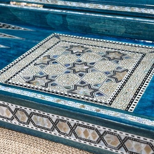 Puede incluir: Un tablero de backgammon de madera azul con un diseño de incrustaciones blancas y negras. El tablero está decorado con incrustaciones de nácar.