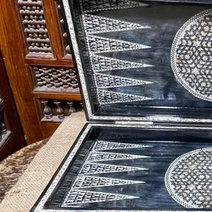 May include: A black and white backgammon board with intricate inlaid mother-of-pearl designs. The board is open and the playing surface is visible.