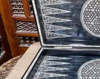 May include: A black and white backgammon board with intricate inlaid mother-of-pearl designs. The board is open and the playing surface is visible.