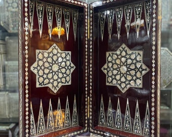 May include: A wooden backgammon board with intricate inlaid mother-of-pearl designs. The board is open and shows the playing surface with the traditional triangular points.