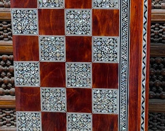 May include: A wooden chessboard with a dark brown finish and inlaid mother-of-pearl squares. The board has a decorative border with a geometric pattern.