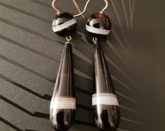 May include: A pair of black and white agate drop earrings with silver hooks. The earrings are made of black agate with white stripes.