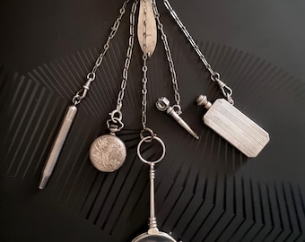 May include: An antique silver chatelaine with various attachments, including a pocket watch, magnifying glass, perfume bottle, pencil, and other decorative items. The pieces are suspended from chains and a decorative top piece.