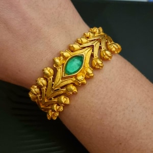 Peut inclure: Un bracelet en or avec une pierre précieuse verte au centre. Le bracelet est composé d'une série de petites formes de fleurs.