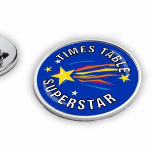 May include: A blue and silver Times Table Superstar badge. The badge has a yellow star with a comet tail design and the words "TIMES TABLE SUPERSTAR" in white text. The badge has a pin back for attachment.