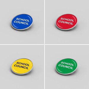 Op de afbeelding: Vier ronde pinnen met zilveren metalen frames. De pinnen zijn blauw, rood, geel en groen. Elke pin heeft de tekst "SCHOOL COUNCIL" in witte letters.