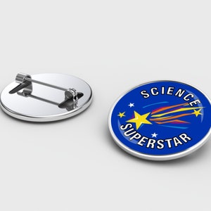 May include: Two round, silver-coloured metal pin badges. One badge has a blue background with the words "SCIENCE SUPERSTAR" and a yellow star with a comet design. The other badge shows the pin's back.