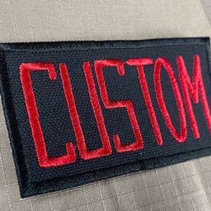 May include: Black rectangular patch with red embroidered text that reads "CUSTOM".