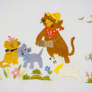 May include: Embroidered image of four cats in a field of flowers. One cat is wearing a hat and playing an accordion. Another cat is wearing a pink bow. The cats are all white, brown, yellow, and gray.