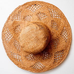 May include: A brown woven straw sun hat with a wide brim and a woven pattern. The hat has a large, open weave.