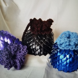May include: Three crocheted drawstring bags with a scale-like design. The bags are purple, black, and blue.