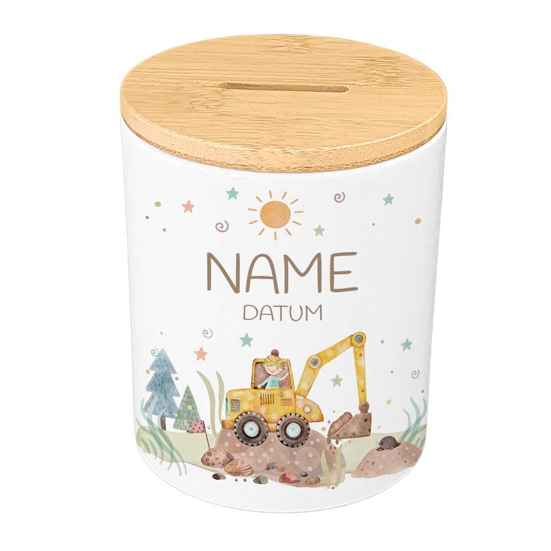 May include: White ceramic money bank with a wooden lid. The bank features a colorful illustration of a yellow excavator, trees, and the text "NAME DATUM". The design includes stars, a sun, and swirls.