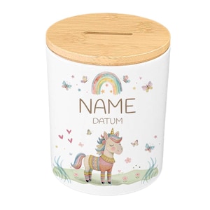 May include: White ceramic money bank with a bamboo lid. The bank features a colorful unicorn, rainbow, butterflies, and the words "NAME" and "DATUM". The design is whimsical and suitable for children.