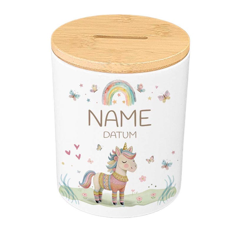 May include: White ceramic money bank with a bamboo lid. The bank features a colorful unicorn, rainbow, butterflies, and the words "NAME" and "DATUM". The design is whimsical and suitable for children.