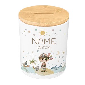May include: White ceramic money bank with a bamboo lid. The bank features a pirate-themed illustration with a pirate boy, treasure chest, and a shark. The text "NAME" and "DATUM" are printed on the bank.