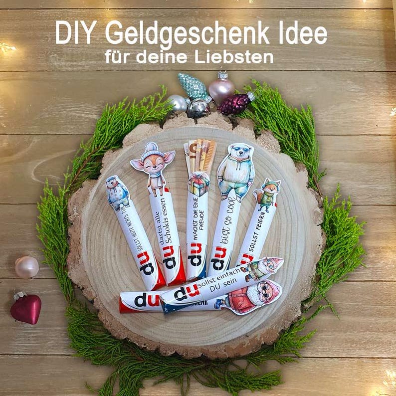 May include: A festive arrangement featuring decorated candy bars with animal-themed toppers, arranged on a wooden slice with greenery and ornaments. The text "DIY Geldgeschenk Idee" is visible at the top.