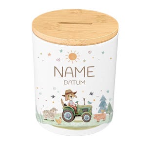 May include: White ceramic piggy bank with a bamboo lid. The bank features a farm scene with a dog driving a green tractor, along with sheep, a pig, and chickens. The text "NAME" and "DATUM" are printed on the bank.