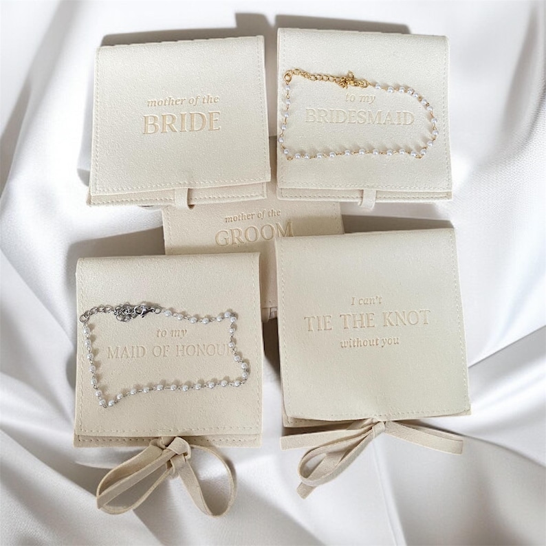Puede incluir: Cajas de regalo de joyer&iacute;a de color crema con texto en relieve, incluyendo "Mother of the Bride", "To my Bridesmaid", "Mother of the Groom", "To my Maid of Honour" y "I can't tie the knot without you". Algunas cajas contienen collares.