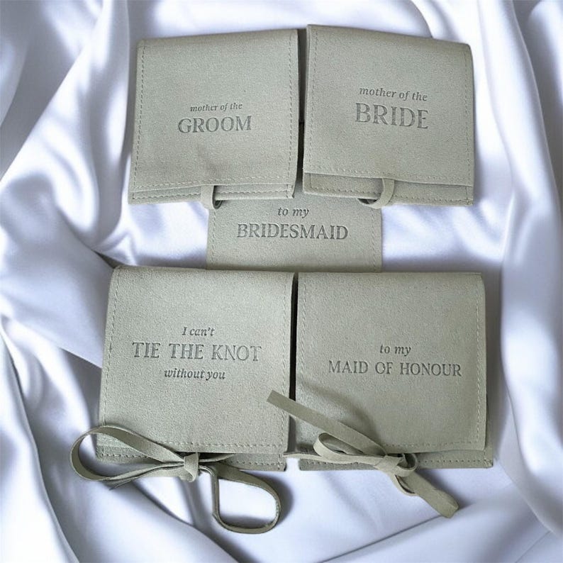 Puede incluir: Una colecci&oacute;n de bolsos cuadrados de color beige claro con texto grabado y lazos a juego. El texto en los bolsos dice: "mother of the GROOM", "mother of the BRIDE", "to my BRIDESMAID", "I can't TIE THE KNOT without you" y "to my MAID OF HONOUR".