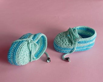 Könnte beinhalten: Ein Paar gehäkelte Babyschuhe in Blau und Grün mit einem gestreiften Muster. Die Schuhe haben Schnürsenkel und sind mit schwarzen Perlen gebunden.