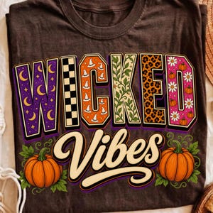 May include: A dark brown t-shirt featuring the text WICKED VIBES in large, multi-patterned block letters. The letters include purple moons, black and white checkers, orange witch hats, green vines, leopard print, and pink daisies with pumpkins.