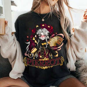 Op de afbeelding: Zwart sweatshirt met een kleurrijke illustratie van een Pierrot-personage met speelkaarten. Het ontwerp bevat een narrenkap, harten en het woord "PIERROT". Het personage heeft wit haar en een ondeugende uitdrukking.