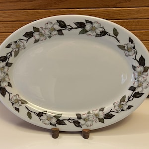 May include: White oval serving platter with a floral design of white dogwood blossoms and green leaves around the rim.