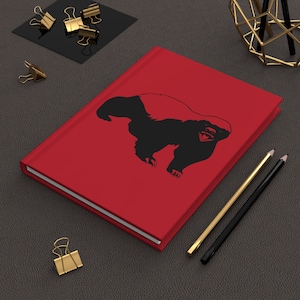 Può includere: Diario con copertina rigida rossa con una silhouette nera di un tasso mellifero sulla copertina.
