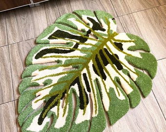 May include: A green and white rug shaped like a large tropical leaf. The rug has a textured, fluffy surface.
