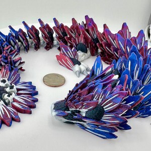 Puede incluir: Esculturas florales abstractas impresas en 3D en tonos de azul, rojo y blanco. Las piezas están dispuestas sobre una superficie blanca, con una moneda como escala. Las esculturas tienen un diseño detallado y en capas.