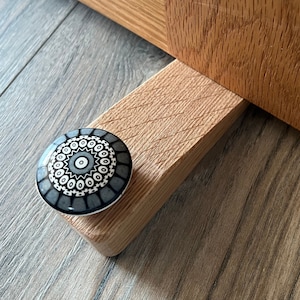 May include: A wooden doorstop with a decorative ceramic knob featuring a black and white geometric pattern.