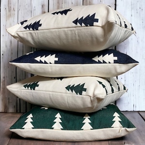 May include: Four decorative throw pillows with a cream-colored background and a repeating pattern of dark green and navy blue stylized Christmas trees.