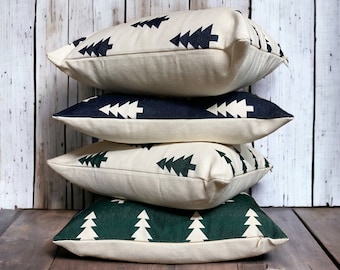 May include: Four decorative throw pillows with a cream-coloured background and a repeating pattern of dark green and navy blue stylised Christmas trees.