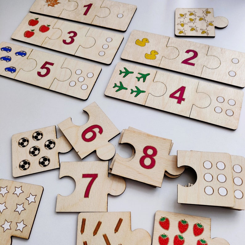 May include: Wooden puzzle pieces with numbers 1 through 8, each piece has a different image, such as apples, airplanes, and soccer balls. The pieces are on a white surface.