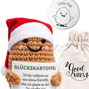 Puede incluir: Una muñeca de patata tejida a ganchillo marrón con un gorro de Papá Noel rojo y blanco, sosteniendo un cartel con el texto GLÜCKSKARTOFFEL, un llavero circular plateado con una ilustración de Little Hug y una bolsa de tela beige con Good Vibes.