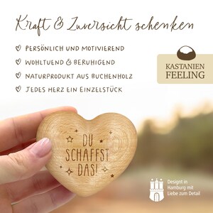 May include: A wooden heart-shaped box with the text "DU SCHAFFST DAS!" engraved on it. The box is held in a hand against a blurred background. The text "KASTANIEN FEELING" is visible in the upper right corner of the image.